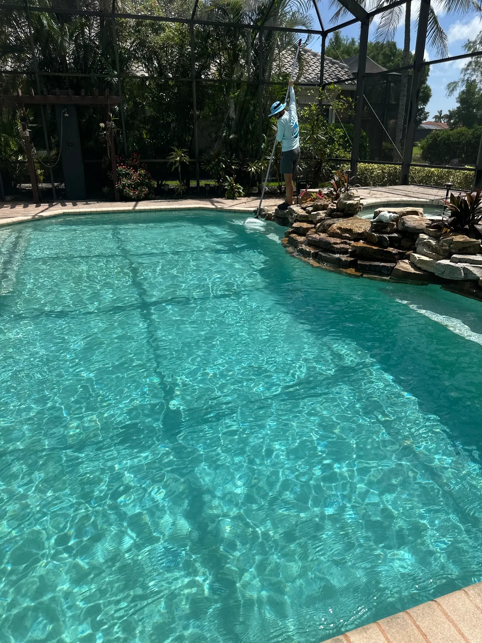 Freeform screened pool with rock waterfall and lush tropical landscaping in Naples, FL