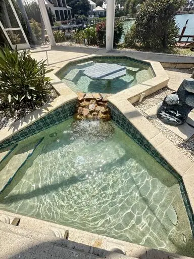 Freeform pool with raised spa and stone waterfall maintained in Bonita Springs, FL