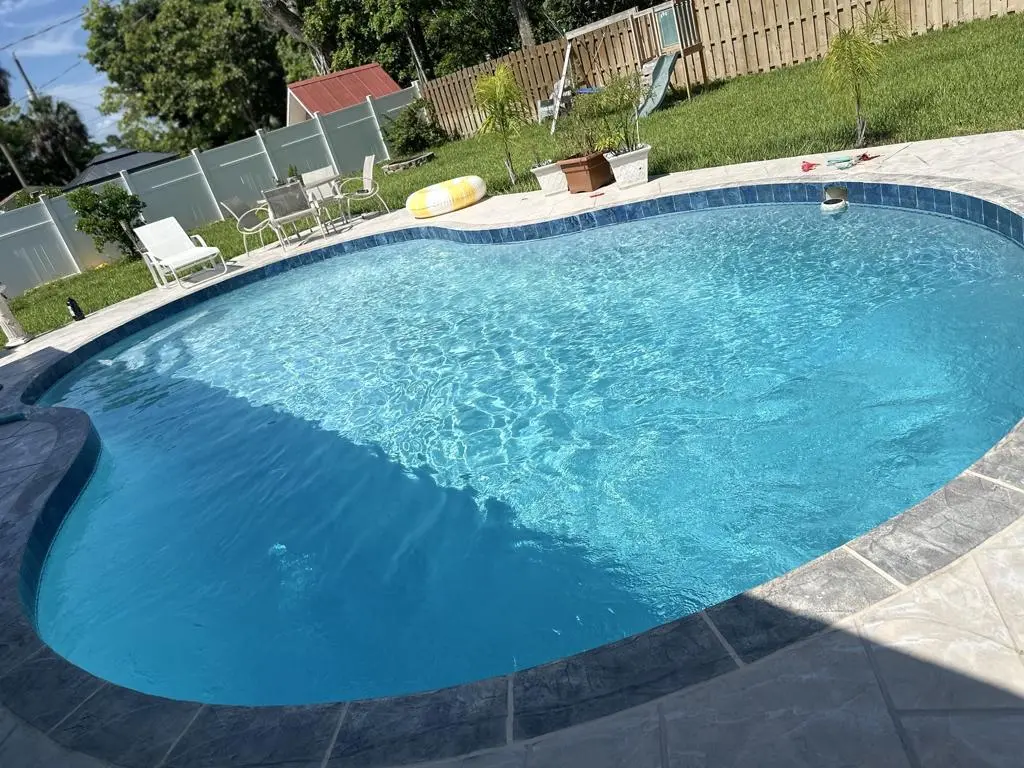 Freeform backyard pool bordered by white fencing and green lawn in Estero, FL