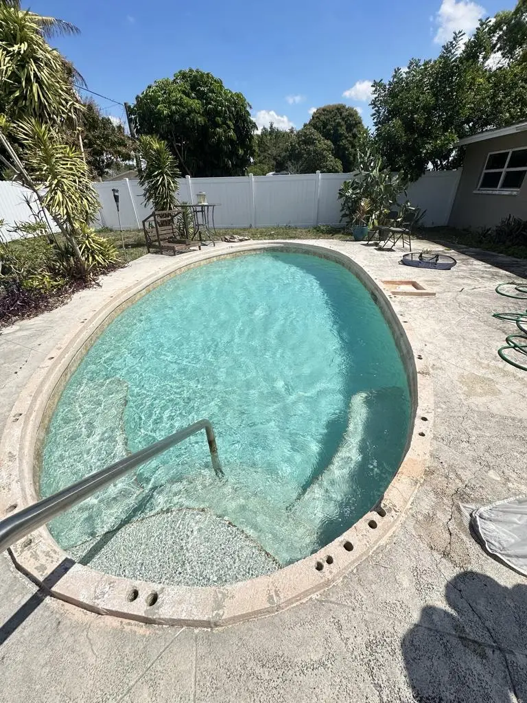 Rounded residential pool with handrail and freshly cleaned concrete deck in Naples, FL