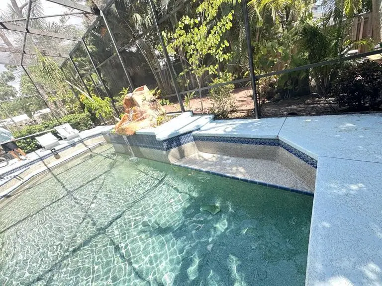 Screened lanai pool with raised spa and rock accent wall after deep tile brushing